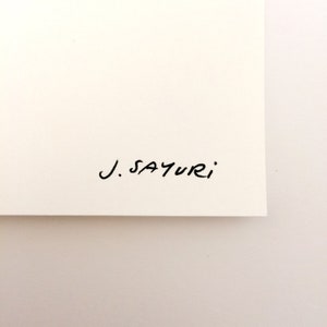 May include: A section of cream-coloured paper with the handwritten signature "J. SAYURI" in black ink. The paper is clean and the signature is in a simple, elegant script.