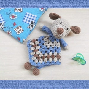 Può includere: Un bavaglino per neonato in crochet grigio e marrone con una coperta blu. Il cucciolo ha un naso marrone e occhi neri. La coperta è un motivo a quadrati della nonna. Il testo "COMFORTER PUPPY" è sul lato sinistro dell'immagine e "CROCHET PATTERN" è sul lato destro dell'immagine.