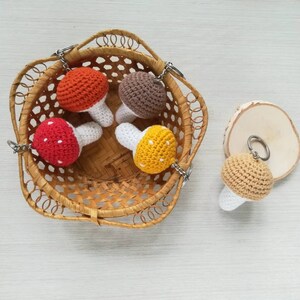 May include: Four crocheted mushroom keychains in a wicker basket. The mushrooms are red with white dots, brown, orange with white dots, and yellow with white dots.