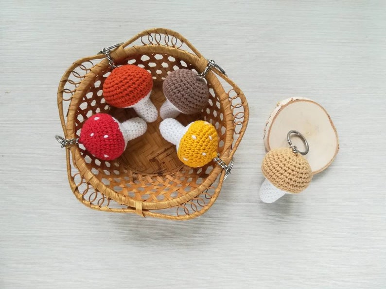 May include: Four crocheted mushroom keychains in a wicker basket. The mushrooms are red with white dots, brown, orange with white dots, and yellow with white dots.