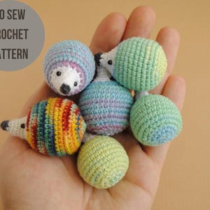 以下が含まれることがあります： 手には、小さなかぎ針編みのハリネズミのおもちゃがいくつかあります。ハリネズミは、青、緑、虹色のストライプなど、さまざまな色です。「NO SEW CROCHET PATTERN」というテキストが、左上の灰色の円の中にあります。