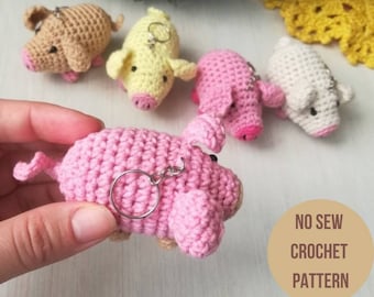 May include: Five crocheted pig keychains in pink, white, yellow, and brown. The keychains are made with a no-sew crochet pattern. "NO SEW CROCHET PATTERN" is written in brown text on a tan background.
