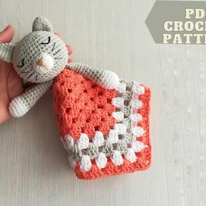 Può includere: Un giocattolo per gatti fatto a mano all'uncinetto con una testa grigia, un naso bianco e una coperta arancione e bianca. Gli occhi del gatto sono chiusi. La coperta è di forma quadrata. Il testo sull'immagine recita "PDF CROCHET PATTERN".