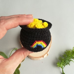 May include: A small crocheted pot of gold with a rainbow design. The pot is filled with yellow crocheted coins.