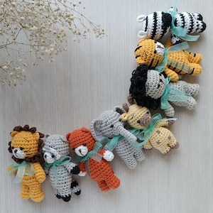 Puede incluir: Una colección de diez peluches de animales de crochet en varios colores, incluyendo una cebra, un tigre, un león, un elefante, una jirafa y un oso. Cada peluche tiene una cinta azul claro atada alrededor de su cuello.