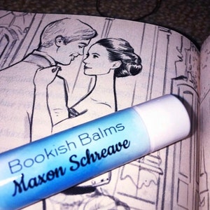 Puede incluir: Un tubo de bálsamo labial azul con tapa blanca y el texto "Bookish Balms Maxon Schreave" impreso en él.