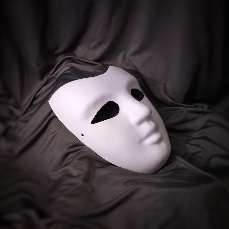 Pu&ograve; includere: Una maschera teatrale bianca con un foro per l'occhio e la bocca chiusa, su uno sfondo di tessuto grigio scuro.