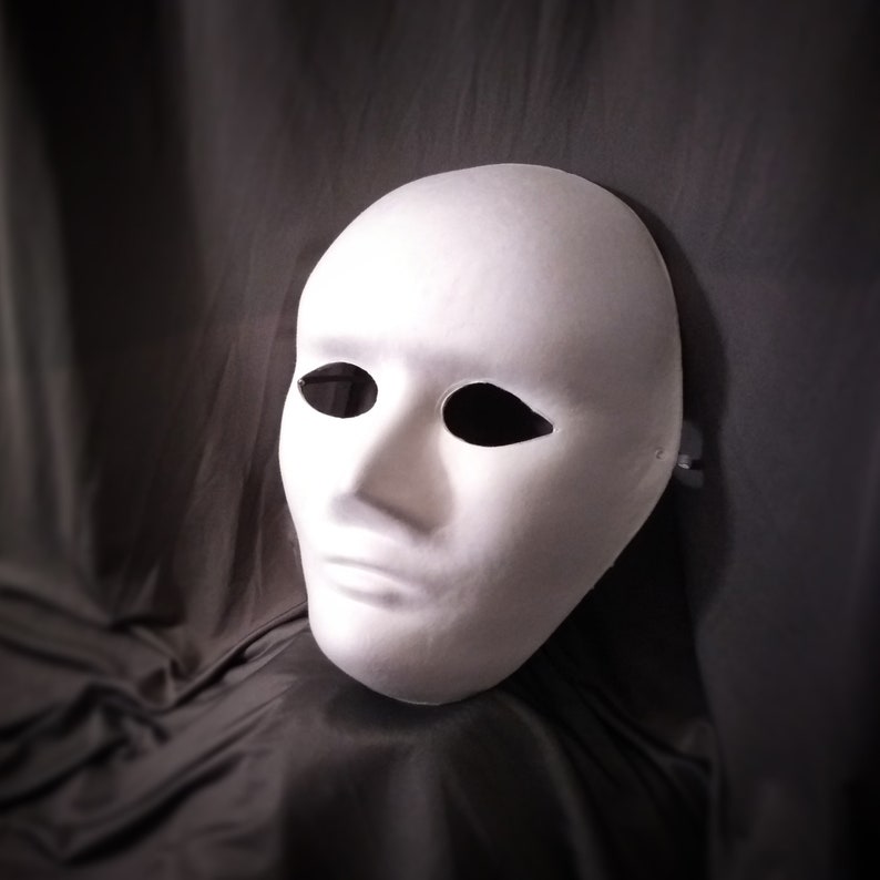 Pu&ograve; includere: Una maschera di carta bianca con due fori per gli occhi e una semplice apertura per la bocca. La maschera &egrave; su uno sfondo grigio scuro.