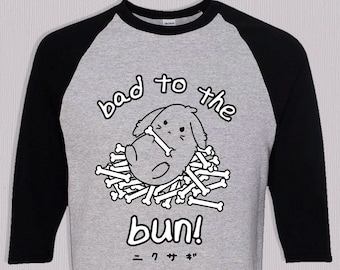 May include: A gray baseball tee with black sleeves featuring a cartoon bunny surrounded by bones. The text "bad to the bun!" is above and below the bunny, with Japanese characters below the text.
