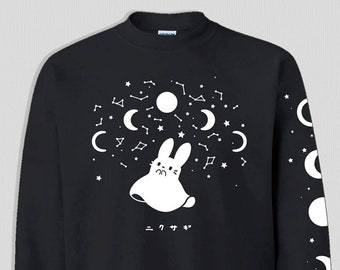 May include: Black sweatshirt featuring a white rabbit design with constellations, moons, and stars. The right sleeve displays moon phases. Japanese text is below the rabbit. A cozy, celestial-themed garment.