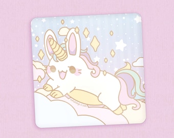 May include: A square sticker featuring a cartoon unicorn-bunny hybrid character with a yellow horn, pink cheeks, and a rainbow tail. The background is light blue with stars and clouds. The sticker is on a pink surface.