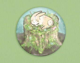 May include: A circular illustration of a sleeping rabbit nestled in a mossy tree stump, surrounded by flowers. The artwork features soft colors, with a light green background and a touch of text at the bottom.