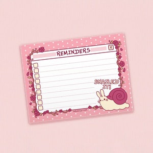 May include: Pink reminder notepad with white polka dots and a floral border. The notepad has a checklist with the word "REMINDERS" at the top. A cartoon snail with a bunny face is on the bottom right corner with the text "SNAILED IT!"