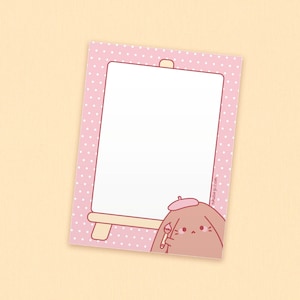 May include: A pink notepad with white polka dots and a white interior. A cartoon bunny wearing a beret and holding a paintbrush is in the lower right corner. The notepad has a small easel design.