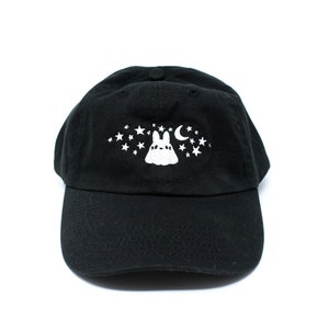 May include: Black baseball cap with a white embroidered design featuring a bunny, stars, and a crescent moon. The cap has a curved brim and an adjustable strap at the back. The hat is made of a soft, durable fabric.
