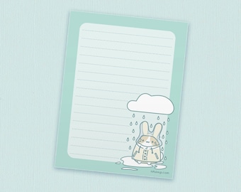 May include: A light blue lined notepad with a cute illustration of a bunny wearing a raincoat standing in a puddle under a cloud with raindrops falling. The text "smudge.ly.com" is at the bottom of the notepad.