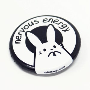 K&ouml;nnte beinhalten: Schwarz-wei&szlig;er Knopf mit einem Comic-Kaninchen und dem Text "nervous energy" am Rand.