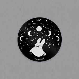 May include: Black and white sticker with a ghost bunny surrounded by stars, moons, and constellations. The sticker has the text "nikusagi.com" at the bottom.