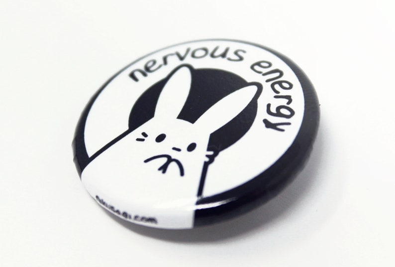 K&ouml;nnte beinhalten: Ein schwarz-wei&szlig;er Knopf mit einem wei&szlig;en Kaninchen mit schwarzem Umriss und dem Text "nervous energy" in einem schwarzen Kreis.