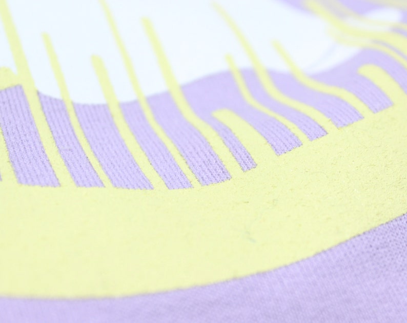 May include: Close-up of a lavender colored fabric with a yellow graphic design. The design is a series of vertical lines that are slightly curved.