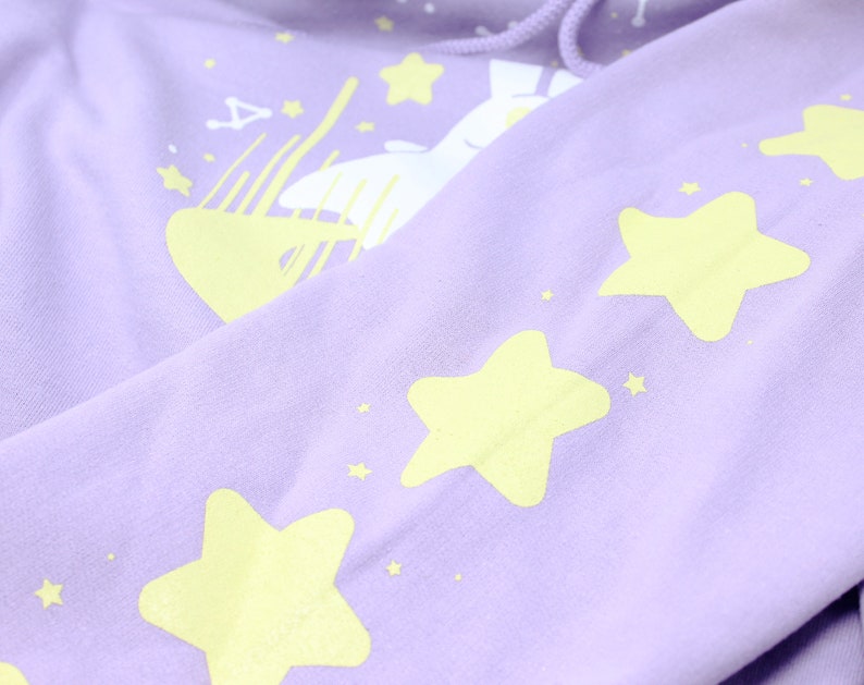 May include: A lavender hoodie with a white bunny and yellow stars printed on it.