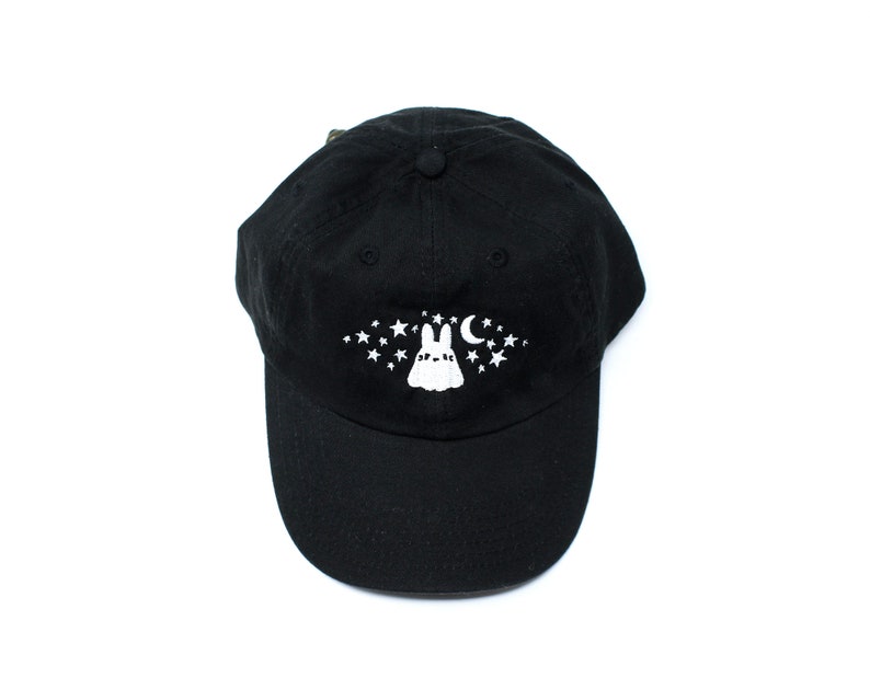 May include: Black baseball cap with a white graphic of a bunny, stars, and a crescent moon. The cap is made of a soft material and has a curved brim. The design is centered on the front of the cap.