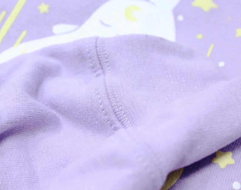 May include: Close-up of the purple fabric of a sweatshirt with a white narwhal design. The fabric is soft and textured.