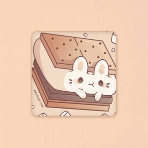 May include: A white bunny peeking out from a chocolate and graham cracker s'more with marshmallows. The s'more is surrounded by white sprinkles on a beige background. The text "nikusagi.com" is printed on the bottom left corner.