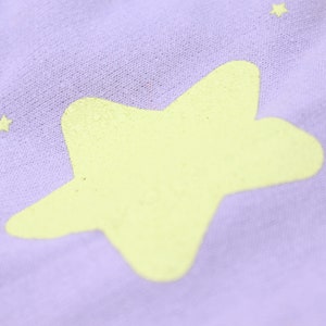 May include: A close-up of a purple fabric with a large yellow star printed on it. The fabric has a soft, textured surface.