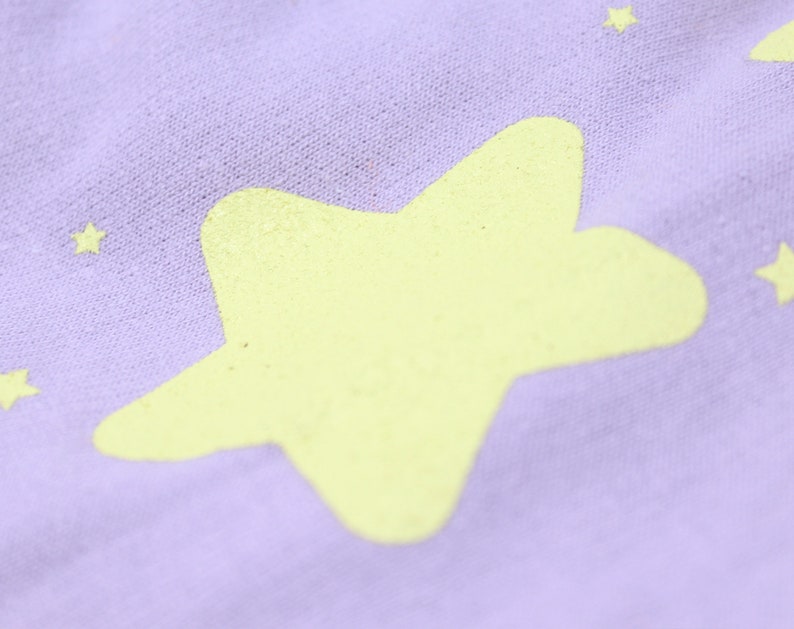 May include: A close-up of a purple fabric with a large yellow star printed on it. The fabric has a soft, textured surface.
