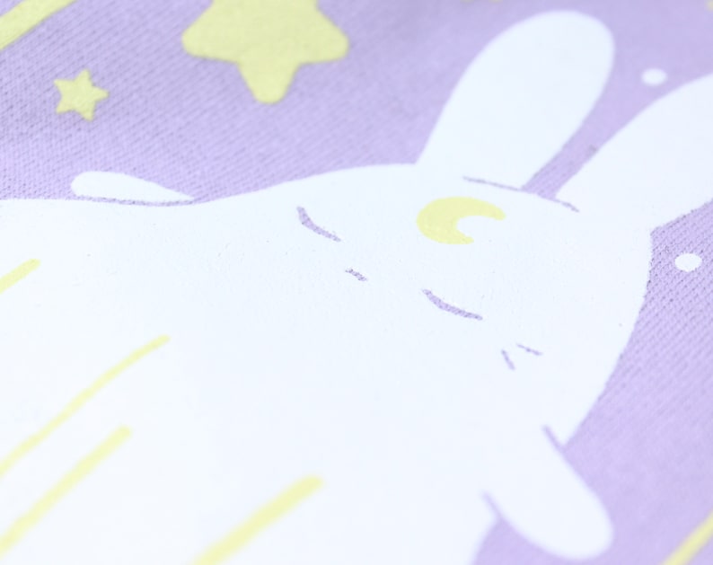 May include: A white bunny with a crescent moon on its forehead is sleeping on a lavender background with yellow stars.