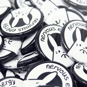 K&ouml;nnte beinhalten: Nahaufnahme einer Stapel schwarzer und wei&szlig;er runder Kn&ouml;pfe mit einem wei&szlig;en Hasen-Motiv und dem Text "nervous energy".