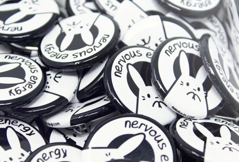 K&ouml;nnte beinhalten: Nahaufnahme einer Stapel schwarzer und wei&szlig;er runder Kn&ouml;pfe mit einem wei&szlig;en Hasen-Motiv und dem Text "nervous energy".