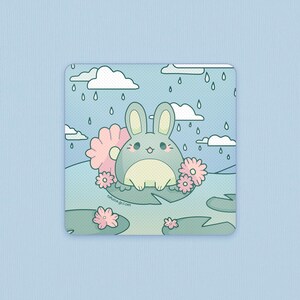 May include: A blue bunny with pink ears sits on a green lily pad surrounded by pink flowers. The background is a blue sky with white clouds and rain drops.