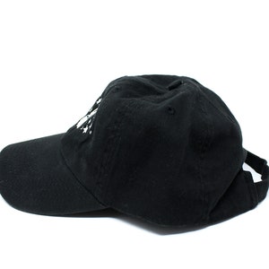 May include: A black baseball cap with a curved brim and adjustable strap. The cap has a white graphic on the front. The hat is made of a soft fabric and is suitable for casual wear.