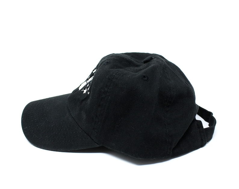 May include: A black baseball cap with a curved brim and adjustable strap. The cap has a white graphic on the front. The hat is made of a soft fabric and is suitable for casual wear.