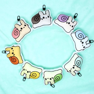 May include: Eight plush snail toys in various colors, each with a different colored shell and a cute cartoon face. The snails are arranged in a circle on a light blue background.
