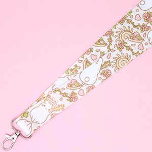 May include: White lanyard with a repeating pattern of bunnies, flowers, hearts, and suns. The lanyard has a silver metal clip.