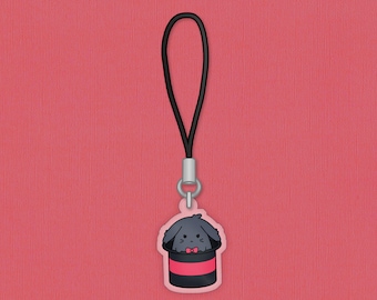 May include: A cartoon-style charm featuring a gray bunny peeking out of a black and red top hat, with a small red bow tie. The charm is attached to a black cord with a silver-colored clasp, set against a pink background.