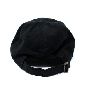 May include: A black baseball cap with a curved brim, viewed from the back. The cap has a fabric strap with a metal buckle for adjustment. The cap is made of a solid, dark fabric.