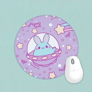 May include: A round mousepad with a cartoon bunny in a spaceship design. The mousepad is lavender with stars, constellations, and a shooting star. A white computer mouse is next to the mousepad. The website nikusagi.com is printed on the mousepad.