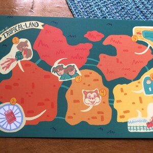 May include: A rectangular print featuring a map titled MAP OF TROPICAL LAND. The map displays seven numbered locations on a dark green background with orange and yellow landmasses, cartoon characters, a cola can, and a roller coaster track.