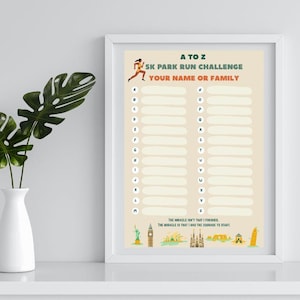 Op de afbeelding: Een ingelijste print met de tekst "A to Z 5K Park Run Challenge" en ruimte om namen te schrijven. De print heeft een beige achtergrond met een hardlopergrafiek en illustraties van bezienswaardigheden. Een witte vaas bevat groene bladeren.