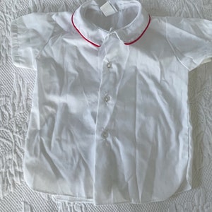 May include: White short-sleeved button-down shirt with a red trim around the collar.