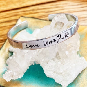 May include: Silver bracelet with the words "Love Wins" engraved on it. A small bee design is also engraved on the bracelet.