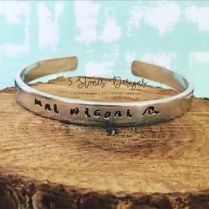 Peut inclure: Bracelet en argent gravé des mots "mal wiiconi" et d'un symbole de vague. Le bracelet est fabriqué par 5 Stones Designs, une entreprise qui grave à la main des porte-clés et des bijoux.