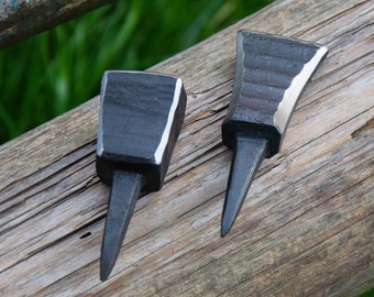 May include: Two black metal tools with pointed tips and a square base. The tools are sitting on a wooden surface.