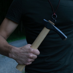 Könnte beinhalten: Eine Person hält eine schwarze und hölzerne Hand-Axt mit einem Holzstiel.
