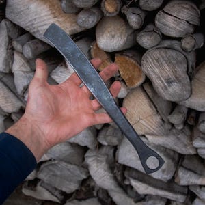 Könnte beinhalten: Eine Hand hält ein schwarzes Metallwerkzeug mit einem abgerundeten Griff und einem Loch in der Mitte. Das Werkzeug ist etwa 30 cm lang und hat eine leicht gebogene Klinge.