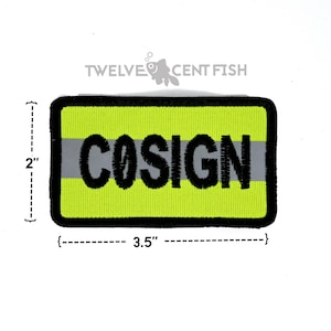 May include: A rectangular neon yellow embroidered patch with a black border and a horizontal gray reflective stripe. The word COSIGN is stitched in black capital letters across the center. The patch measures 2 inches by 3.5 inches.